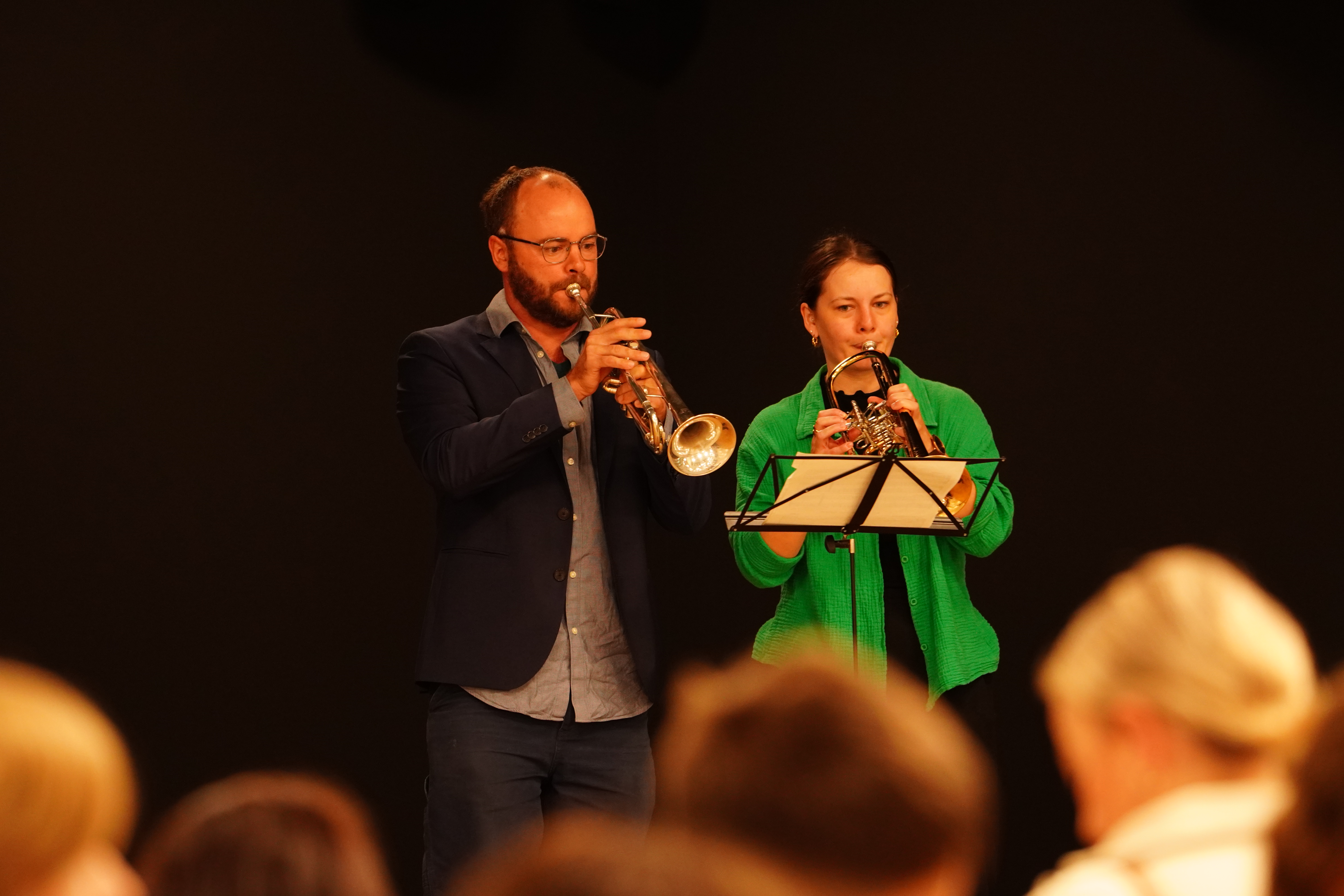 Auf dem Bild sieht man einen Trompeter in schwarzen Sacko und eine Trompeterin in grünem Blazer. 